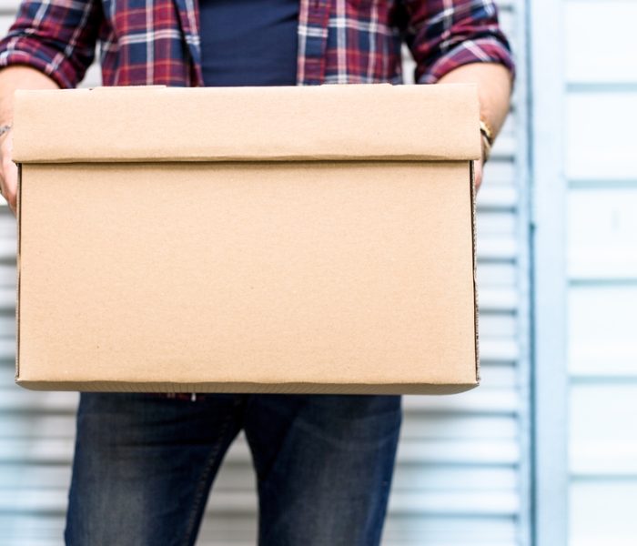 Young,Man,Holding,A,Moving,Cardboard,Box,In,Front,Of